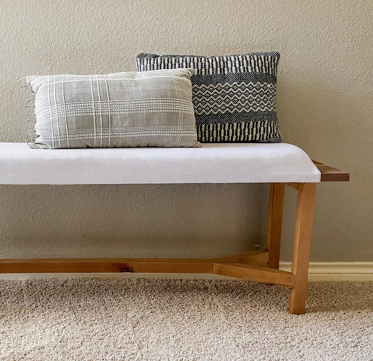 Hand crafted wooden bench with simple upholstered seat and two pillows set on it.
